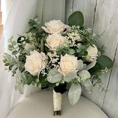 a bouquet of white roses and greenery sits on a chair in front of a window