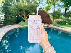 a person holding up a drink in front of a pool with the words, the beach club on it