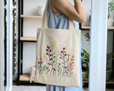 a woman standing in front of a book shelf holding a tote bag with flowers on it