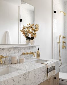 a white bathroom with marble counter tops and gold faucets on the sink vanity