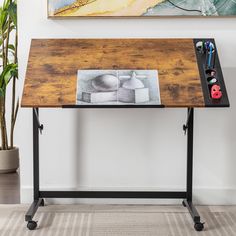 a desk with a drawing on it in front of a painting and pencils next to a potted plant