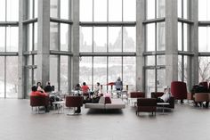 people are sitting and standing in the lobby at an office building with large windows on both sides