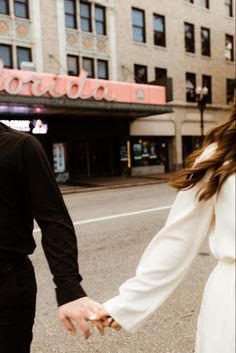 a man and woman holding hands while walking down the street in front of a theater