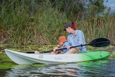 a woman and her child are in a kayak on the water with reeds