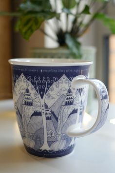 a blue and white cup sitting on top of a table next to a potted plant