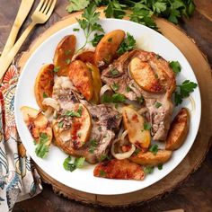 a white plate topped with meat and potatoes next to a fork on a wooden table