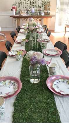 the table is set with plates, cups and flowers in vases on top of moss