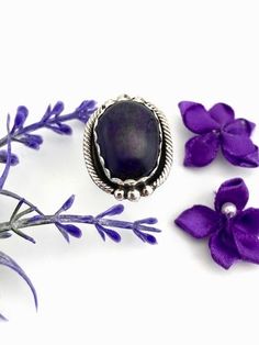 Sugilite is found in shades from light lavender all the way to almost jet black. The cabochon in this pretty ring is some of the deepest purple that still looks purple. The freeform sugilite cabochon is set in an unusual rope trim shadowbox with three bead combination on top and bottom. Geneva Ramone, noted Navajo silversmith, made this cute sterling silver pinky ring. This sugilite pinky ring measures 3/4 of an inch long and 5/8 of any inch wide. It weighs 6.0 grams. Deep in the South African e Purple Amethyst Oval Cabochon Ring, Spiritual Oval Purple Amethyst Ring, Purple Cabochon Amethyst Ring, Oval Purple Amethyst Ring With Natural Stones, Oval Amethyst Ring With Natural Stones, Silver Pinky Ring, Floral Cuff, Spark Up, Pretty Ring