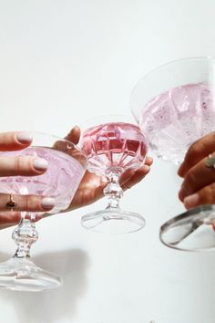 three people holding wine glasses with pink liquid in them