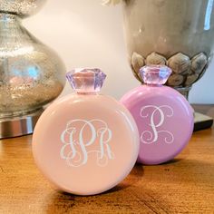 two pink and purple perfume bottles sitting on top of a wooden table next to a vase