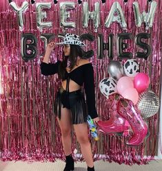 a woman standing in front of a pink backdrop with balloons and streamers on it