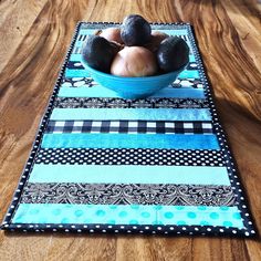 a bowl filled with fruit sitting on top of a wooden table covered in blue and black fabric