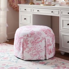 a pink and white flowered ottoman sits in front of a vanity