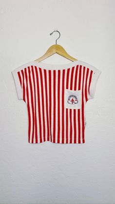 "70s vintage red and white striped crop shirt with capped sleeves and front logo pocket on left breast.  Soft poly cotton blend fabric, high neck, and cap sleeves make this the perfect summer top s i z e small m e a s u r e m e n t s bust: 30\" waist: 28\" length: 16\" sts: 32\" al: 14\" m a t e r i a l poly / cotton blend c o n d i t i o n good vintage; some signs of fading and wear c a r e machine wash delicate hang or tumble dry low" Red Cropped Cotton T-shirt, White Summer Tops With Vertical Stripes, White Vertical Stripes Summer Tops, Red Retro Top With Graphic Print, White Retro Print Top For Summer, White Vertical Stripes Top For Spring, White Tops With Vertical Stripes For Spring, White Relaxed Fit Top With Striped Hem, Retro Cotton Summer Tops