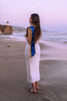 a woman standing on top of a sandy beach next to the ocean wearing a white dress