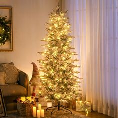 a lit christmas tree in front of a window with candles on the floor next to it