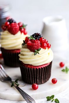 two cupcakes with white frosting and fresh berries on top are sitting on a plate