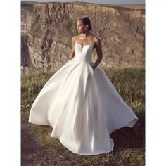 a woman in a white wedding dress standing on the edge of a cliff looking off into the distance