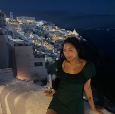 a woman standing on top of a roof next to a city at night with buildings in the background