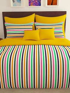 a bed with yellow sheets and colorful striped comforter set on top of the bed