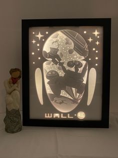 a small figurine sitting next to a framed wallpaper with the word wall e on it