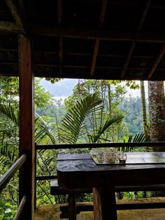 a wooden table sitting on top of a porch next to a lush green forest filled with trees