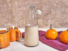 two mugs and a bottle are sitting on a towel next to some pumpkins