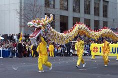 two men in yellow outfits are dancing with a dragon on the street while people watch