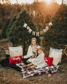 a woman and two children sitting on a blanket in front of a christmas tree at sunset