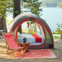 a tent set up in the woods with a table and chairs next to it, overlooking a body of water