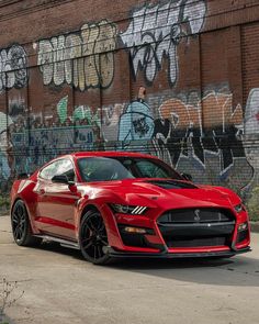 a red sports car parked in front of a brick wall with graffitti on it