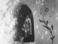 the virgin mary statue is next to a wall with flowers and vines painted on it