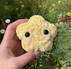 a hand holding a small stuffed animal in front of some wildflowers and flowers