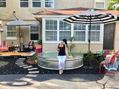 a woman sitting in an outdoor hot tub next to a patio with chairs and umbrellas