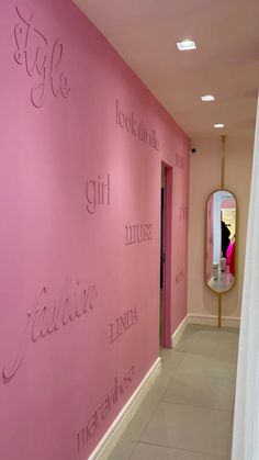 a pink wall with writing on it and a mirror in the hallway next to it