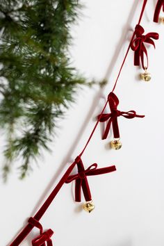 red ribbon with bells hanging from it on a white wall next to a pine tree