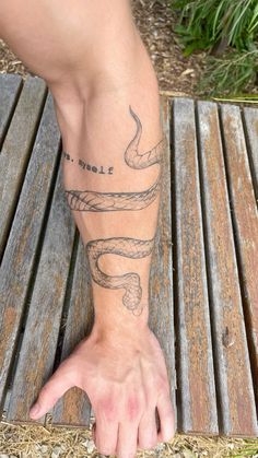 a person's arm with a snake tattoo on it, sitting on a wooden bench