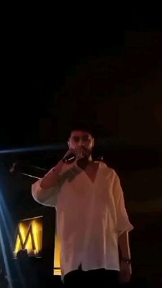 a man standing on top of a stage holding a cell phone to his ear while wearing a white shirt