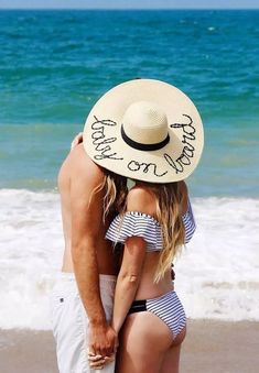 a man and woman standing on top of a beach next to the ocean wearing hats