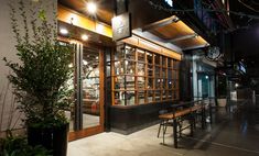 the outside of a restaurant at night with lights on and plants in pots next to it