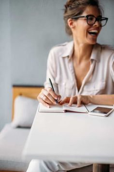 a woman sitting at a table with a pen in her hand and writing on a notepad