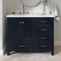 a white sink sitting under a mirror next to a blue cabinet with gold handles and drawers