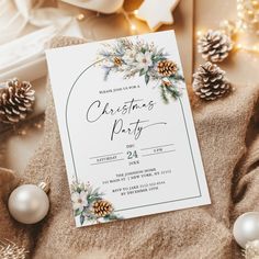 a christmas party card sitting on top of a blanket next to ornaments and pine cones