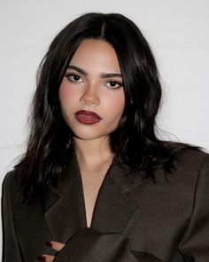 a woman with long dark hair wearing a brown coat and lipstick on her lips, posing for the camera