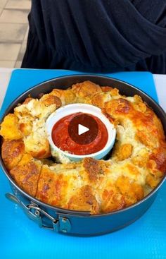 a pizza in a pan with sauce on top and a woman sitting at a table behind it