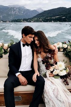 a man and woman sitting on a boat in front of the water with flowers around them