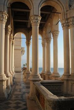 an old building with columns and tiled flooring next to the ocean on a sunny day