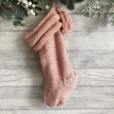 a knitted stocking hanging on a wooden wall next to flowers and greenery