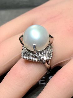 A large and impressive cocktail ring centered by a prong set 14.75mm white South Sea pearl with a very slight silver undertone exhibiting an even luster with extremely minor surface pitting. Surrounding the pearl is approximately 2.20cttw in H-I color Vs2-Si1 clarity round and baguette diamonds. Dimensions/Weight: Ring measures 1" in diameter and weighs 15.6g. Size 6 (sizable). Condition: All stones are secure and in perfectly wearable condition. R-OPPJ Luxury Round Cut Cubic Zirconia Pearl Ring, White Diamond Rings For Evening, White Oval Baguette Diamond Jewelry, Luxury White Rings For Evening, Classic White Evening Rings, Luxury White Evening Rings, White Baguette Cut Jewelry For Evening, White Pearl Ring With 17 Jewels For Formal Occasions, Formal White Pearl Ring With High Luster