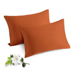 two orange pillow cases with white flowers on the side and one is in front of them